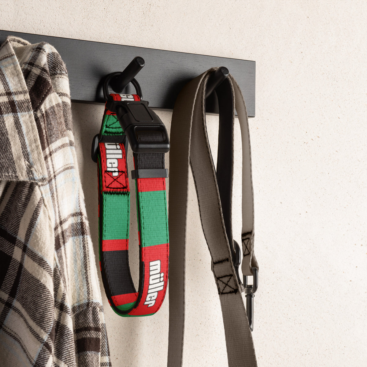 Black, red & green football dog collar hanging on a wall hook with a shirt and leash