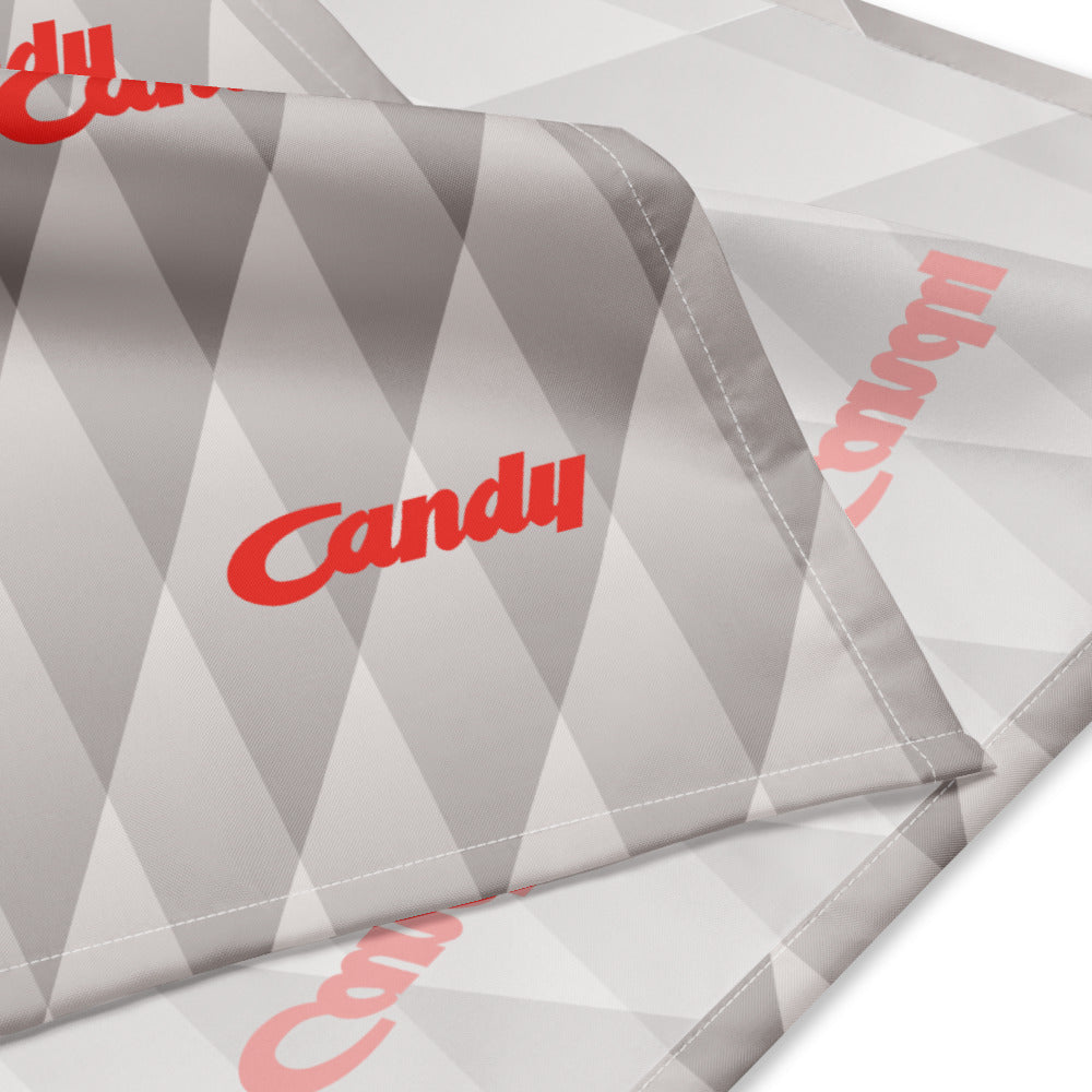 A close-up of a gray and white geometric patterned fabric with the word 'Candy' printed in red script, folded to show its texture and stitching.