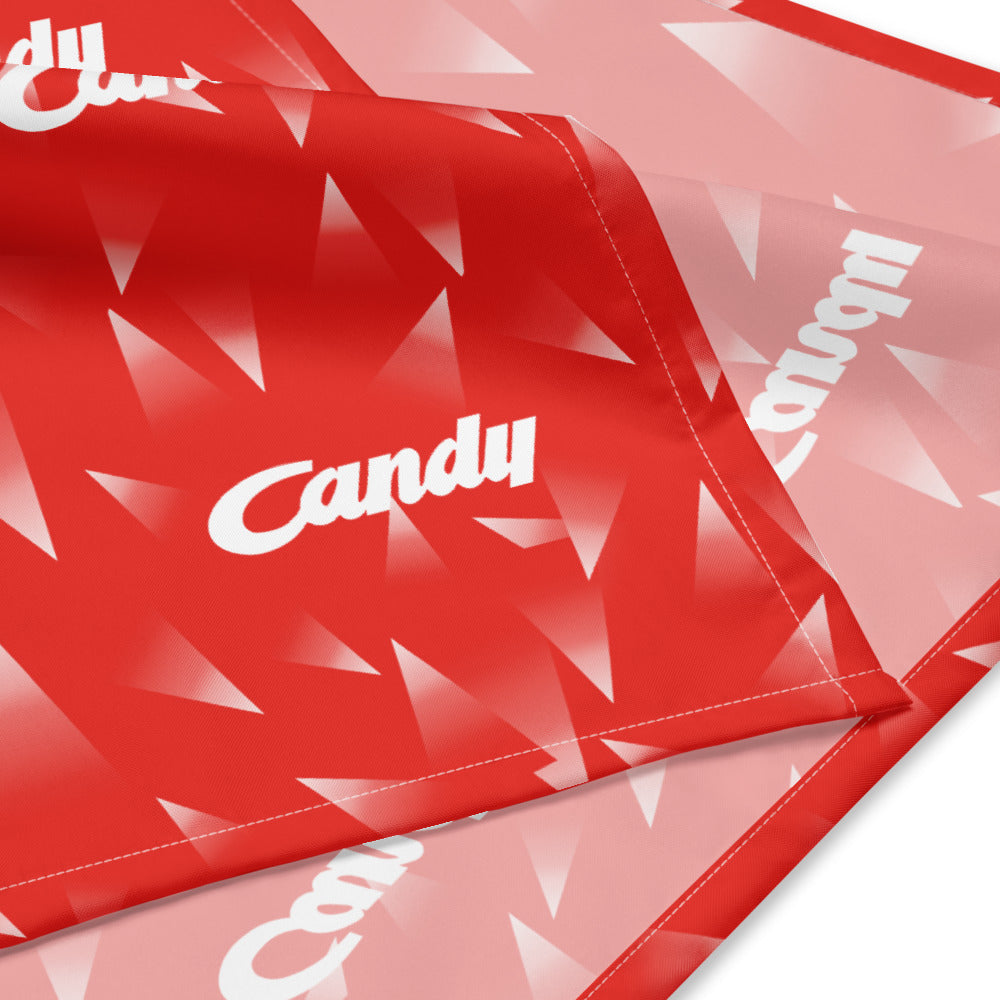 A close-up of a red fabric item, likely a blanket or throw, featuring a geometric triangle pattern and the word 'Candy' printed in white script.