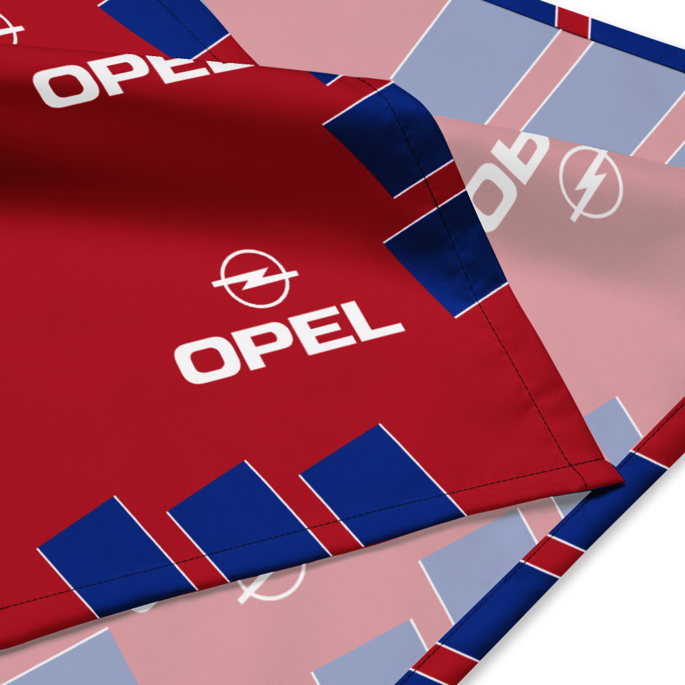 A close-up of a red Opel-branded textile or flag with blue and light pink geometric blocks and repeated white Opel logos, shown folded on a white background.