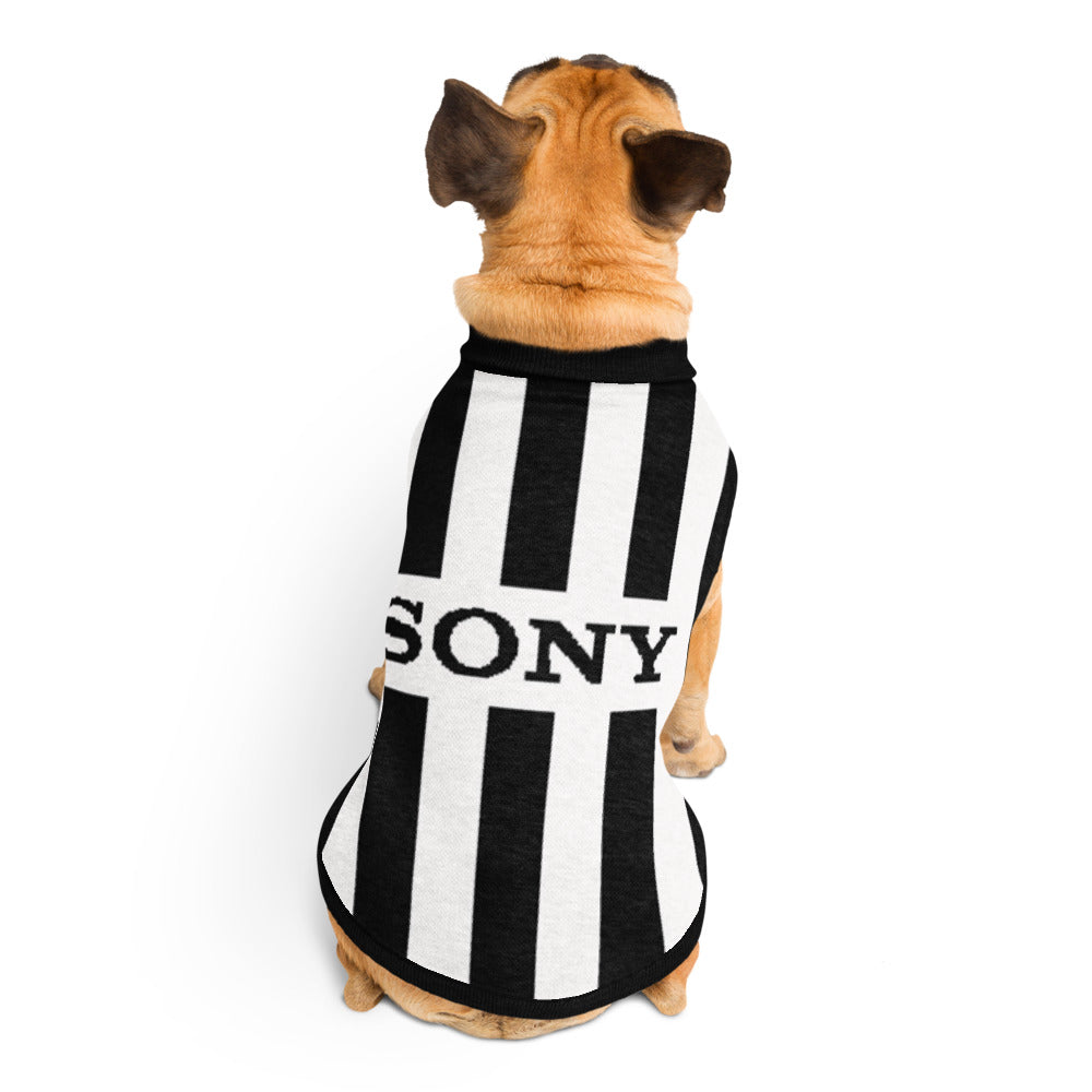 A small tan dog viewed from behind wearing a black and white vertically striped pet shirt with the word 'SONY' printed across the back, on a plain white background.