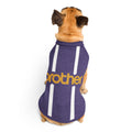 A small tan dog viewed from behind wearing a purple pet shirt with white vertical stripes and yellow 'brother' text across the back, on a plain white background.