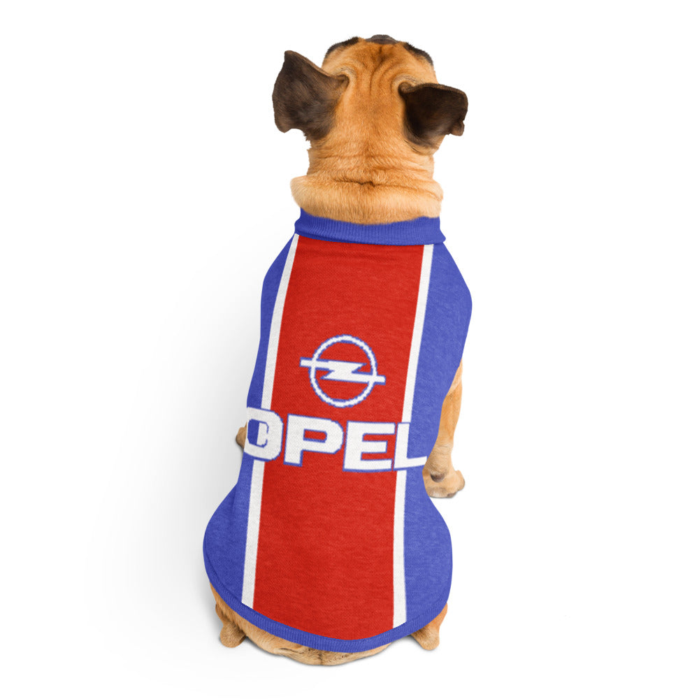 A small tan dog viewed from behind wearing a red, blue, and white pet shirt with the Opel logo and 'OPEL' text on the back, against a plain white background.