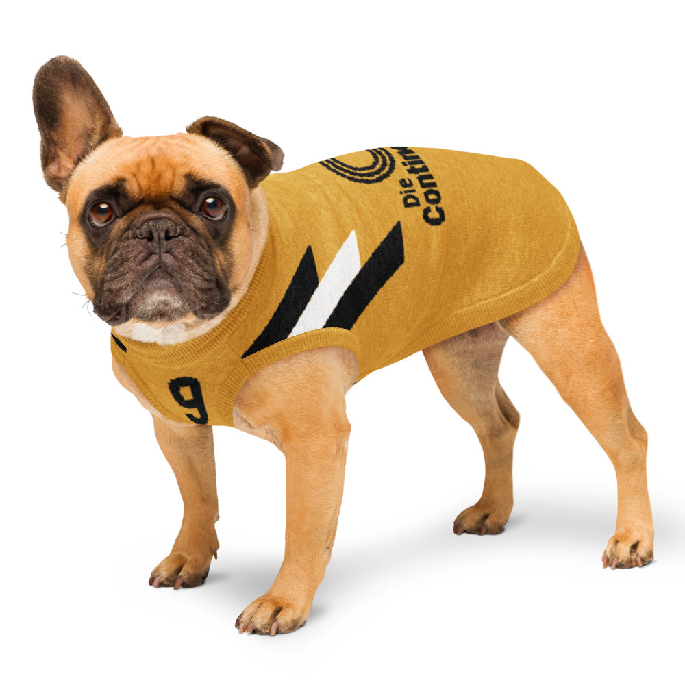 A fawn French Bulldog wearing a mustard yellow knit dog sweater with black and white graphic details and the text 'Die Comic'. The dog is standing against a clean white background.