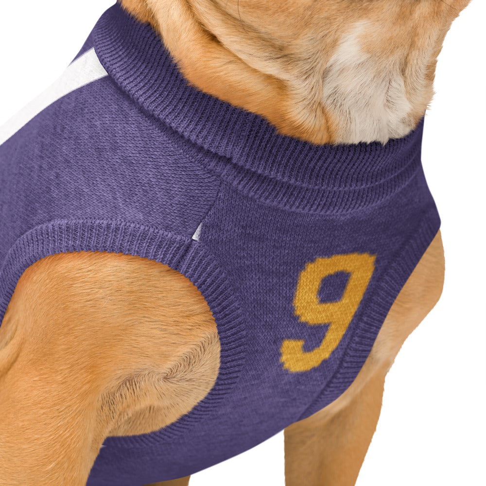 A close-up of a dog wearing a purple knit sweater vest with a yellow number 9 on the side, set against a plain white background.