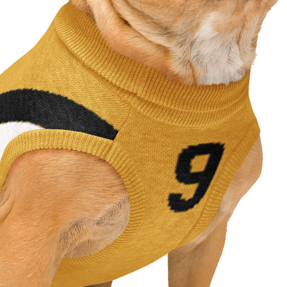 Close-up of a dog wearing a mustard yellow knit sweater with a black number 9 on the side, shown against a plain white background.