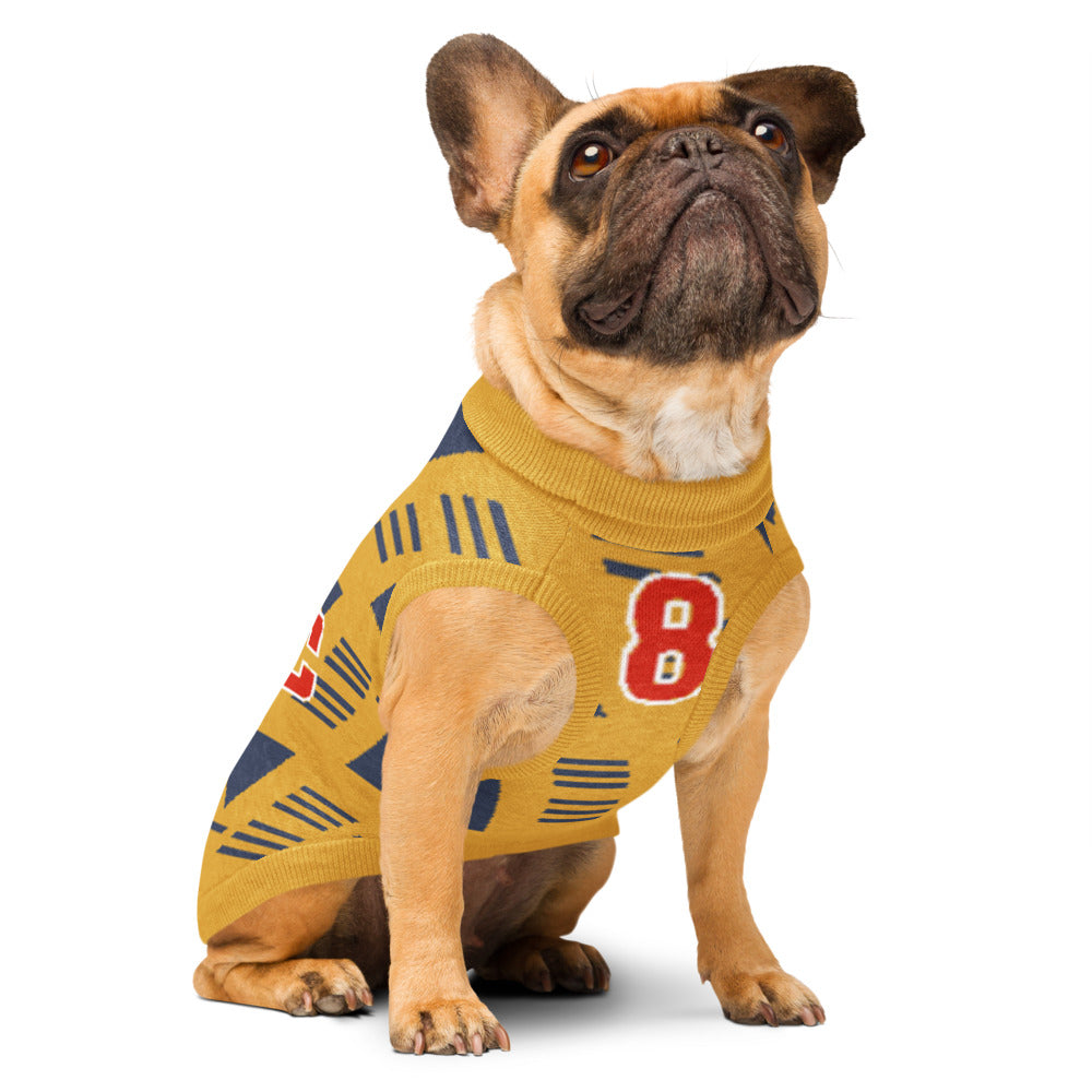 A fawn French bulldog wearing a yellow knit dog sweater with navy blue geometric patterns and a red number 8 on the side, photographed against a solid white background.