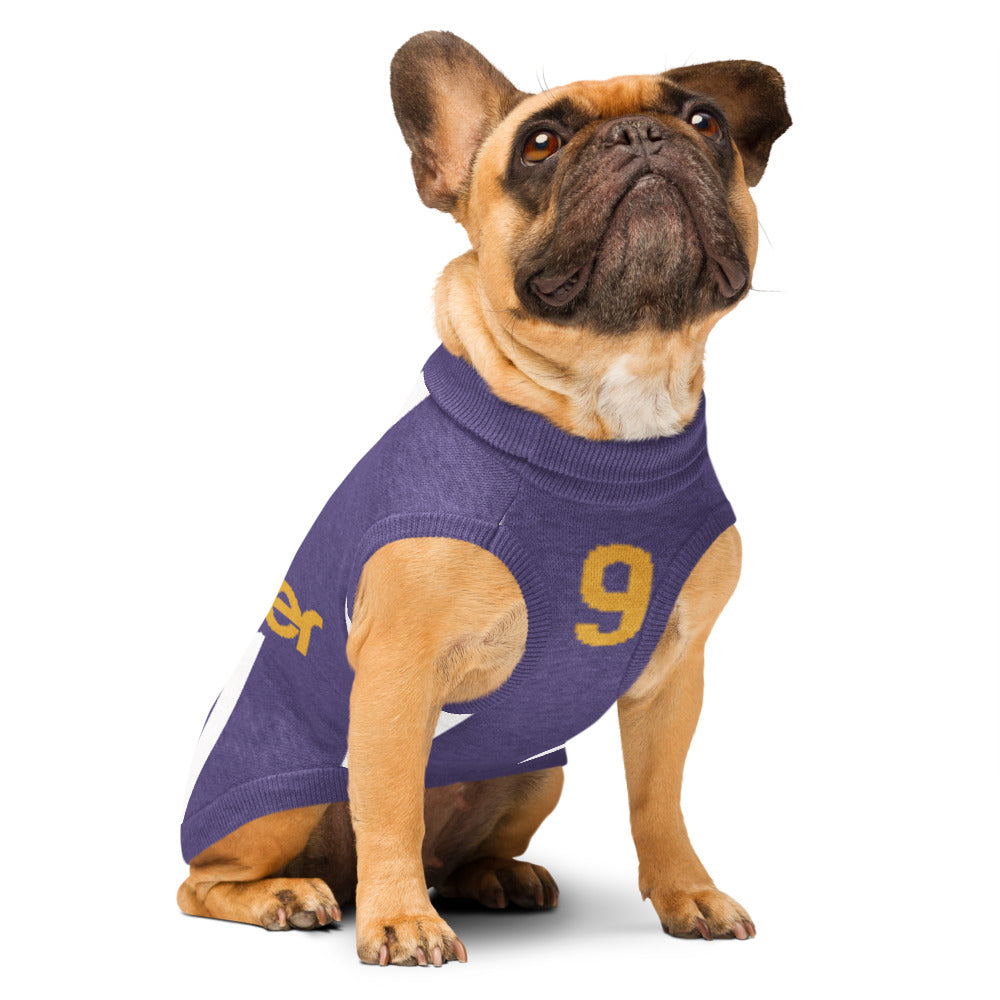 A fawn French Bulldog wearing a purple knit dog sweater with a yellow number 9 on the back, sitting against a solid white background.
