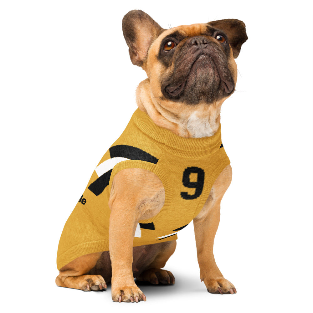 A fawn French bulldog wearing a mustard yellow knit dog sweater with black and white graphic details and the number 9 on the back, photographed against a solid white background.