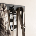A Sony dog collar and matching leash hanging from a black wall hook on a light beige textured wall, next to a plaid shirt.