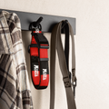 A red and black Motta dog collar hangs on a black wall hook next to a gray strap, with a plaid shirt partially visible on the left, against a light textured wall.