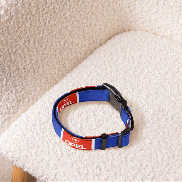 A blue and red dog collar with white branding text, resting on a textured cream boucle armchair.